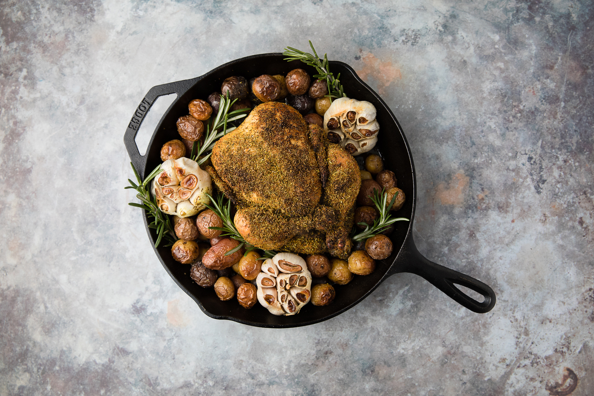 herb rubbed whole chicken in a cast iron skillet on a textured grey background